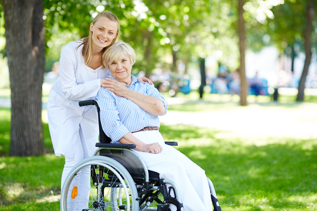 Pretty nurse and senior patient in a wheelchair looking at camera outside
