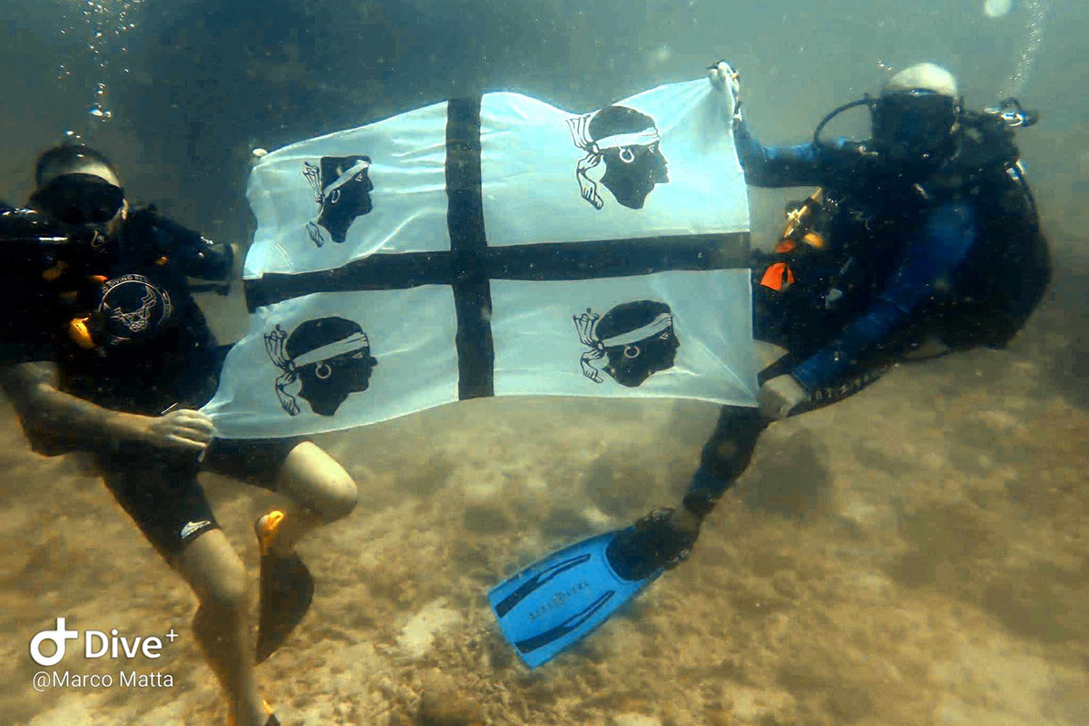 Marco Matta con la bandiera della Sardegna nei fondali tropicali